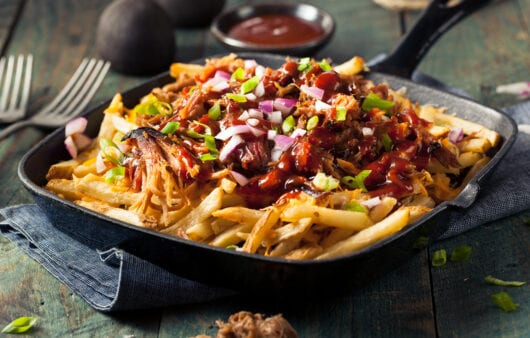 Loaded BBQ pulled pork fries in a skillet with green onions and sauce.