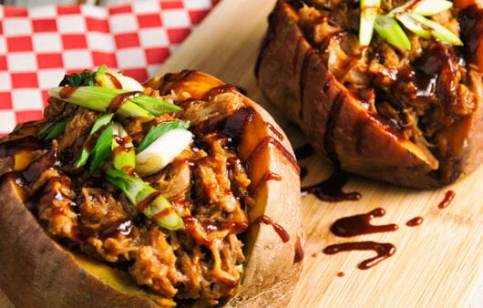 Pulled pork stuffed sweet potatoes on wooden board with garnish