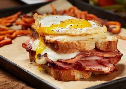 Fried egg and bacon sandwich on sourdough bread with sweet potato fries